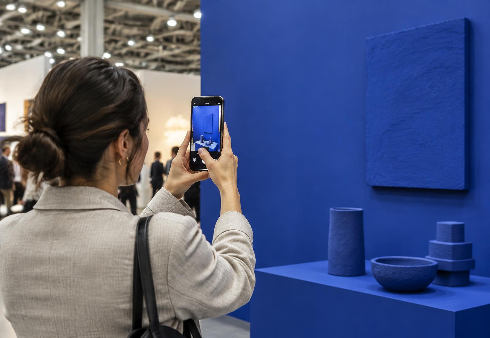 A visitor at a design exhibition holding up her phone to capture a cobalt blue display wall