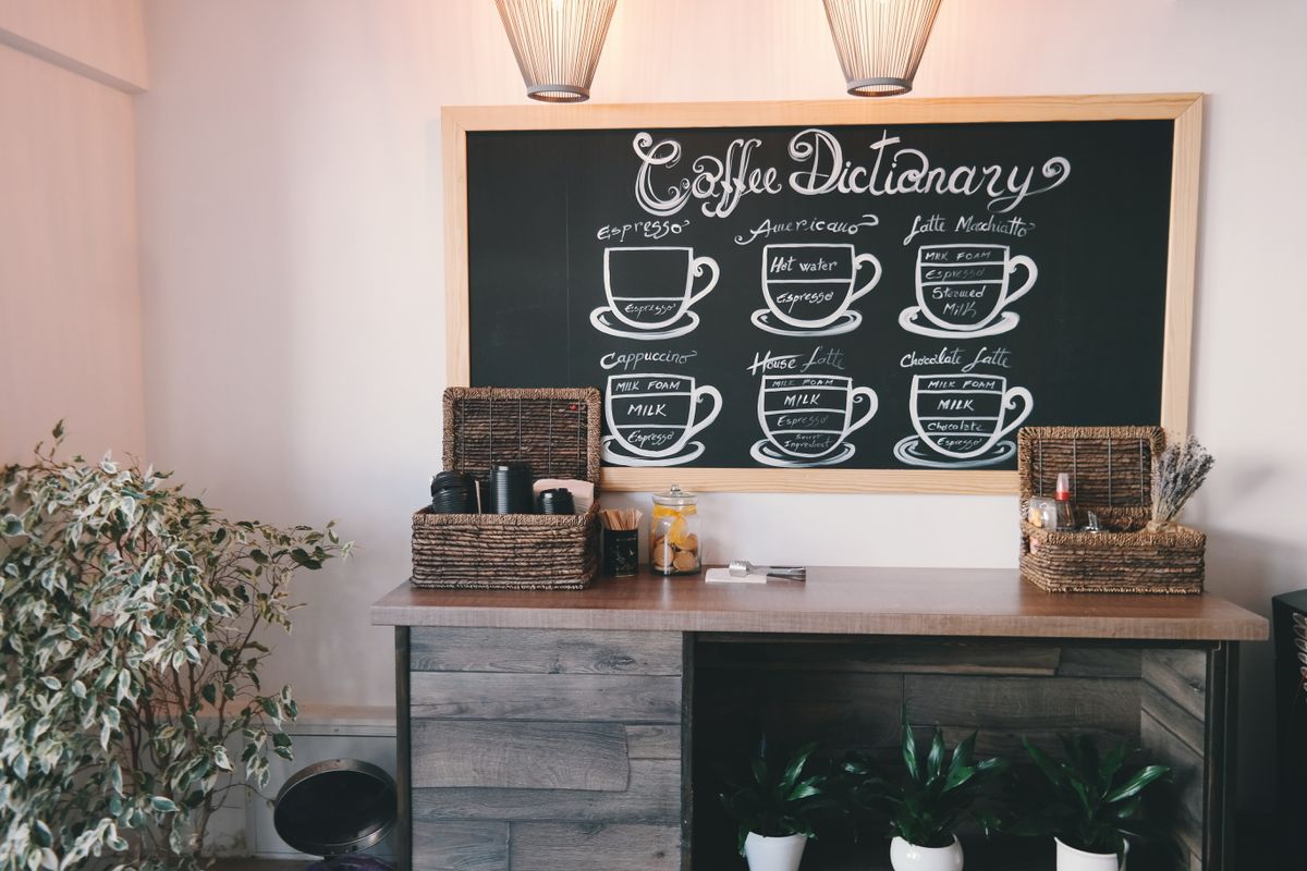 A clearly hand-lettered chalkboard menu board mounted above a cafe counter