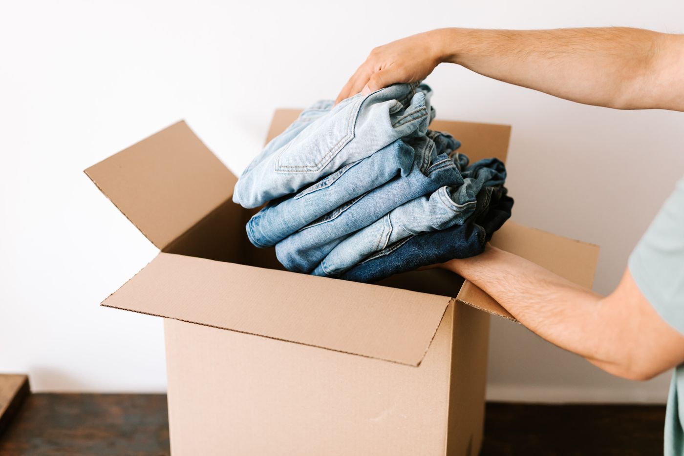Hands folding and packing clothing into a cardboard box ready to post